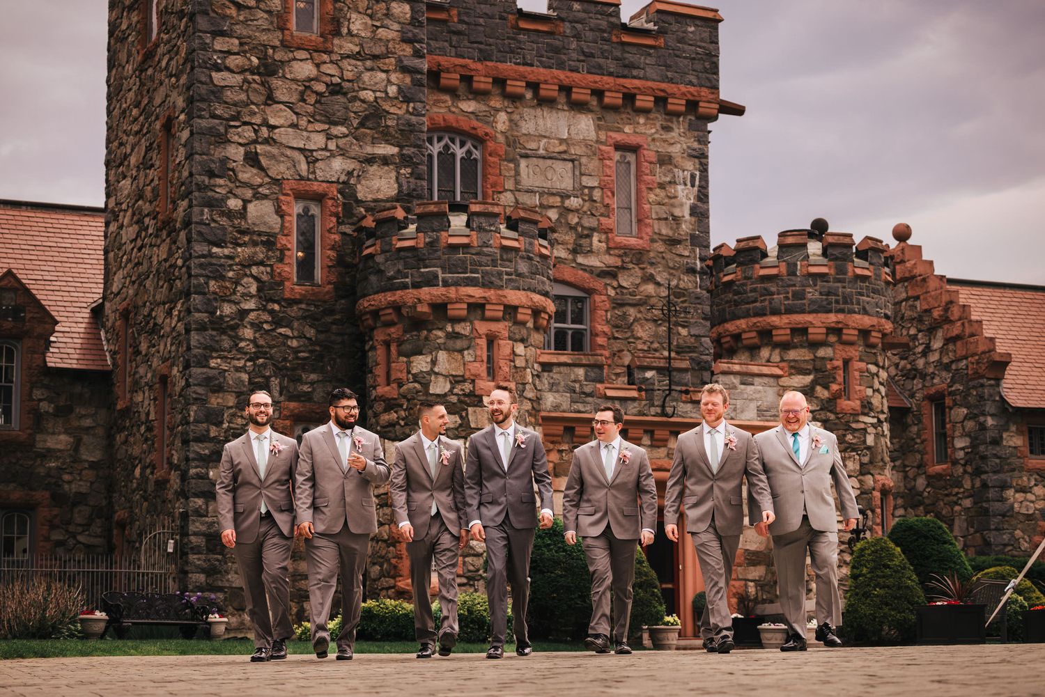 Groom and groomsmen walking together in front of the stone towers of Searles Castle in Windham, New Hampshire