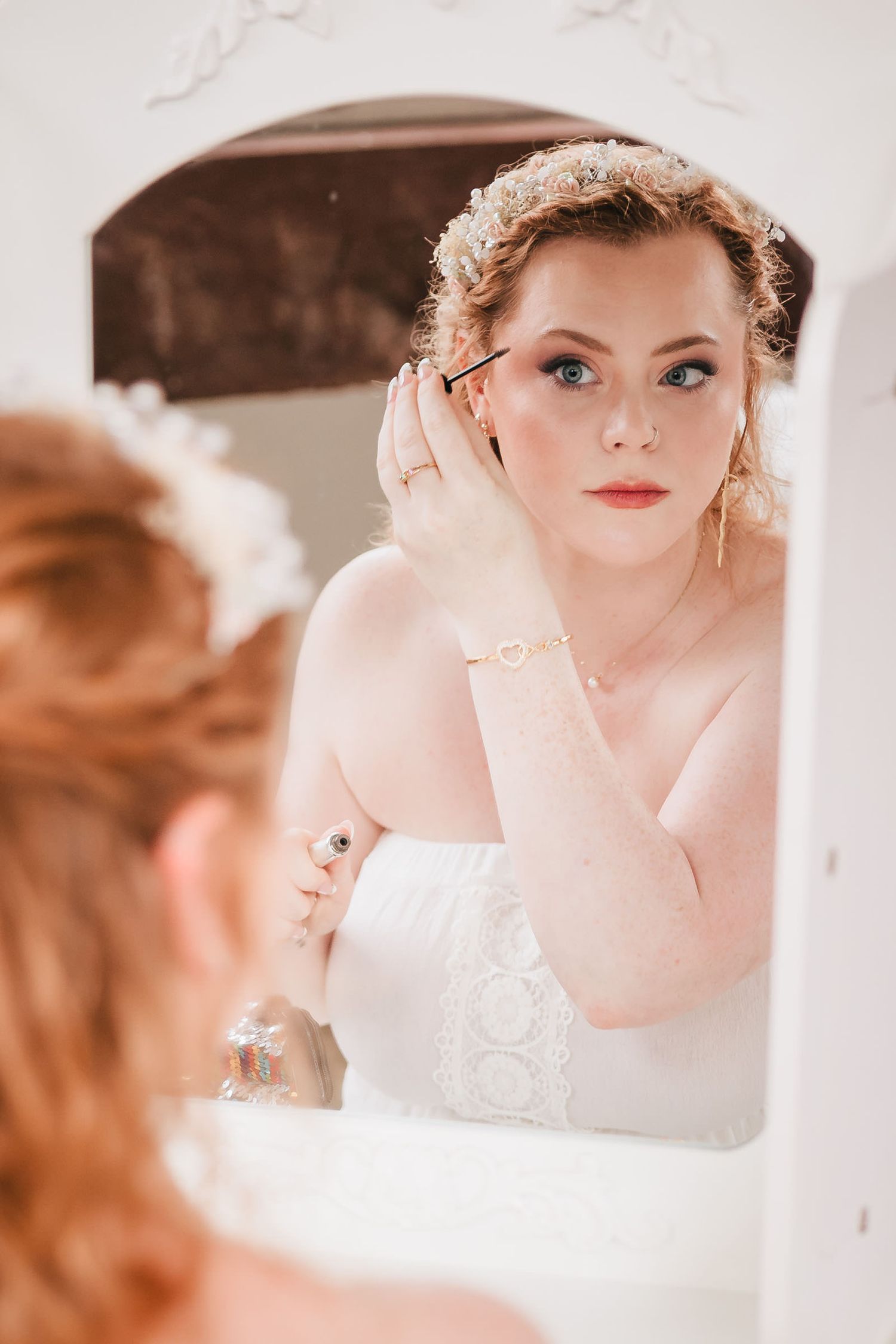 Bride applying eyeliner in a mirror, her reflection and profile both visible, during preparations