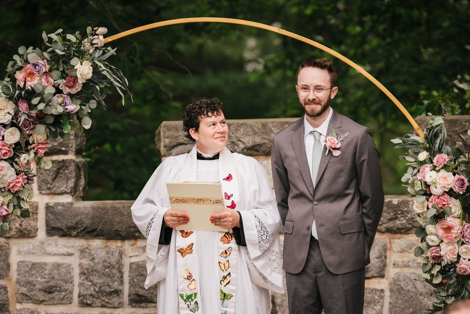 Officiant Joy Caires and the groom waiting at the ceremony arch as the bride arrives.