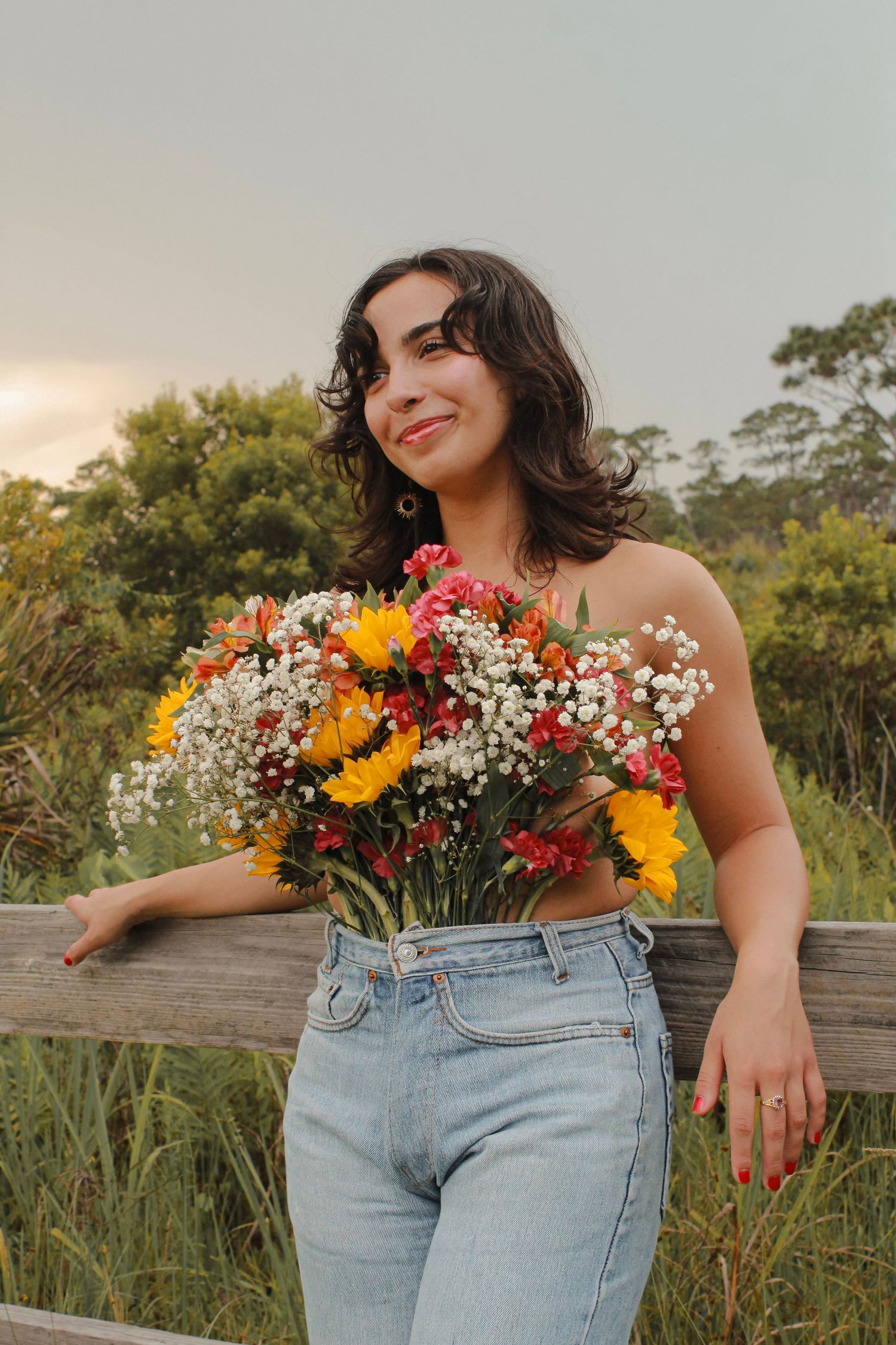 Smiling woman holding a large colorful bouquet of sunflowers and wildflowers outdoors.