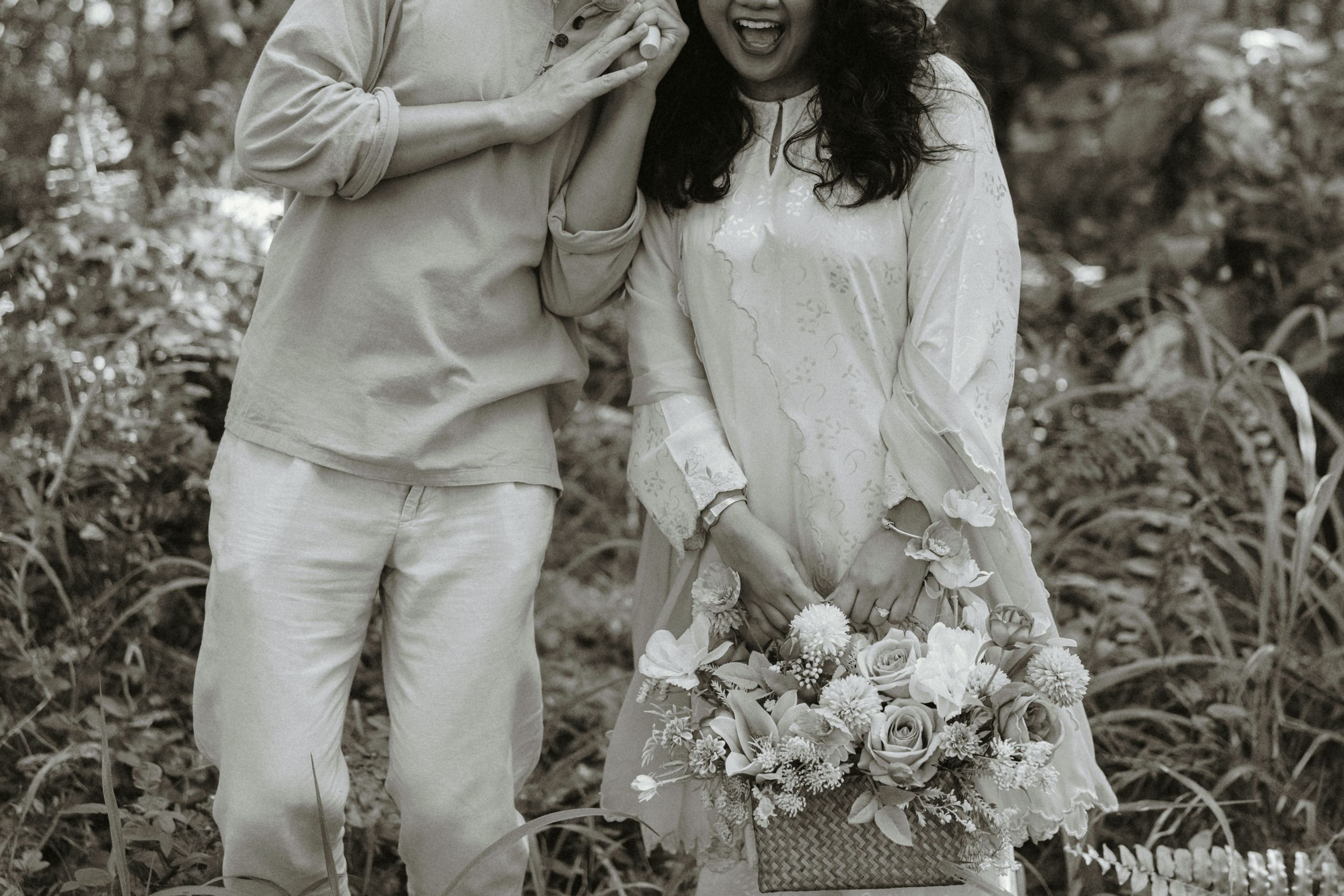 Black and white photo of a couple in a garden, woman holding a floral bouquet basket, smiling joyfully.