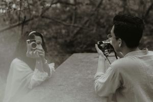 Two people photographing each other with vintage film cameras outdoors in a black and white artistic portrait.