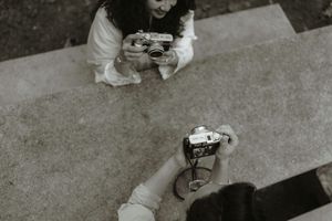 Two people photographing each other with vintage film cameras, captured from an aerial perspective in black and white.