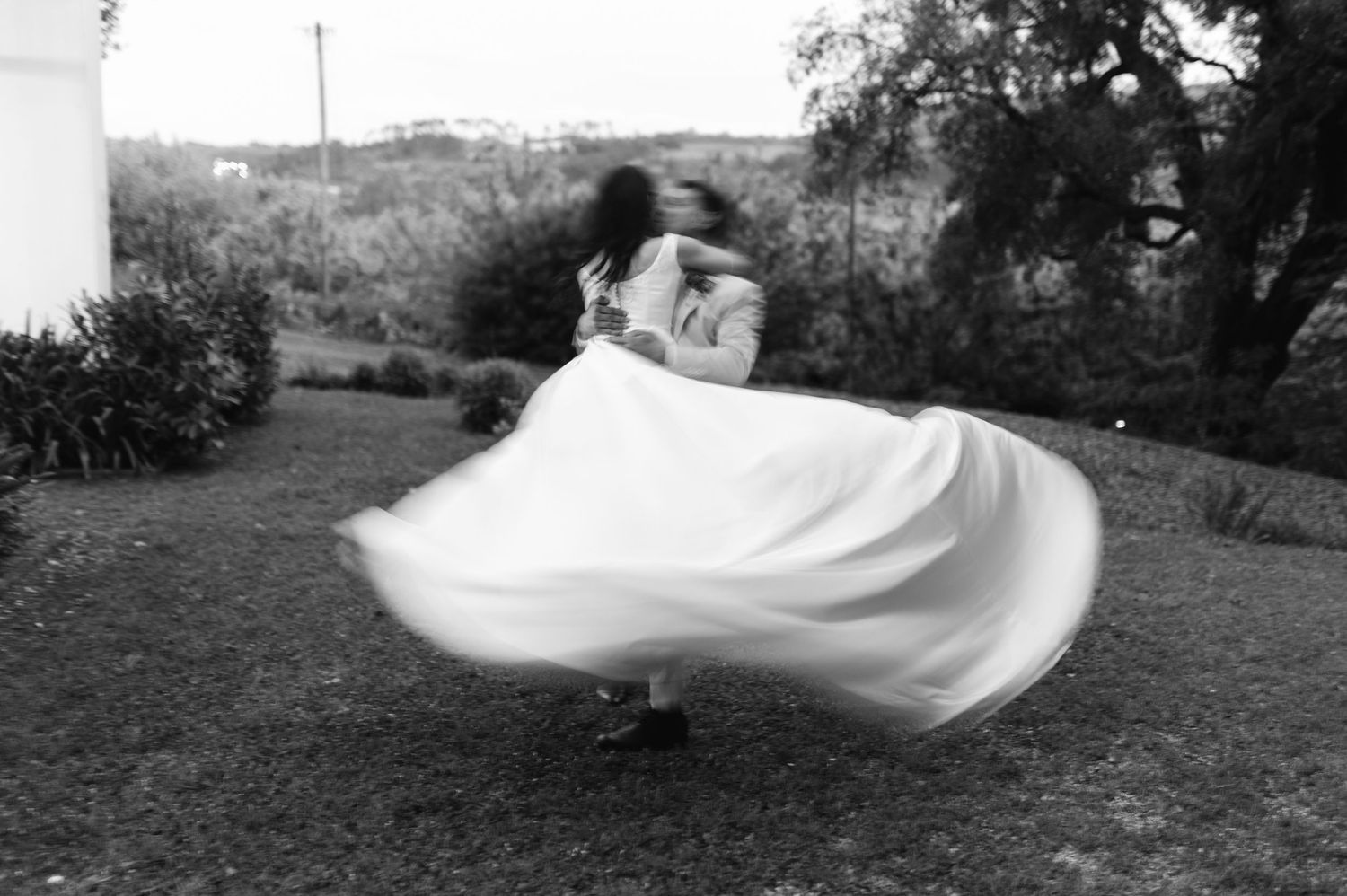 Black and white photo of a bride spinning in a flowing white gown outdoors, captured with motion blur.