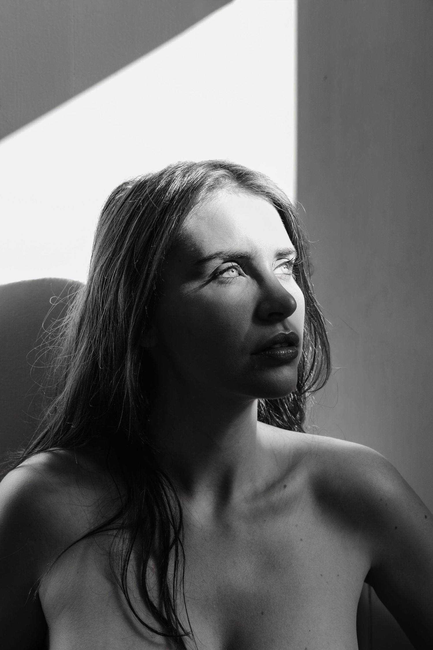 Black and white portrait of a young woman with long hair gazing upward in dramatic studio lighting.
