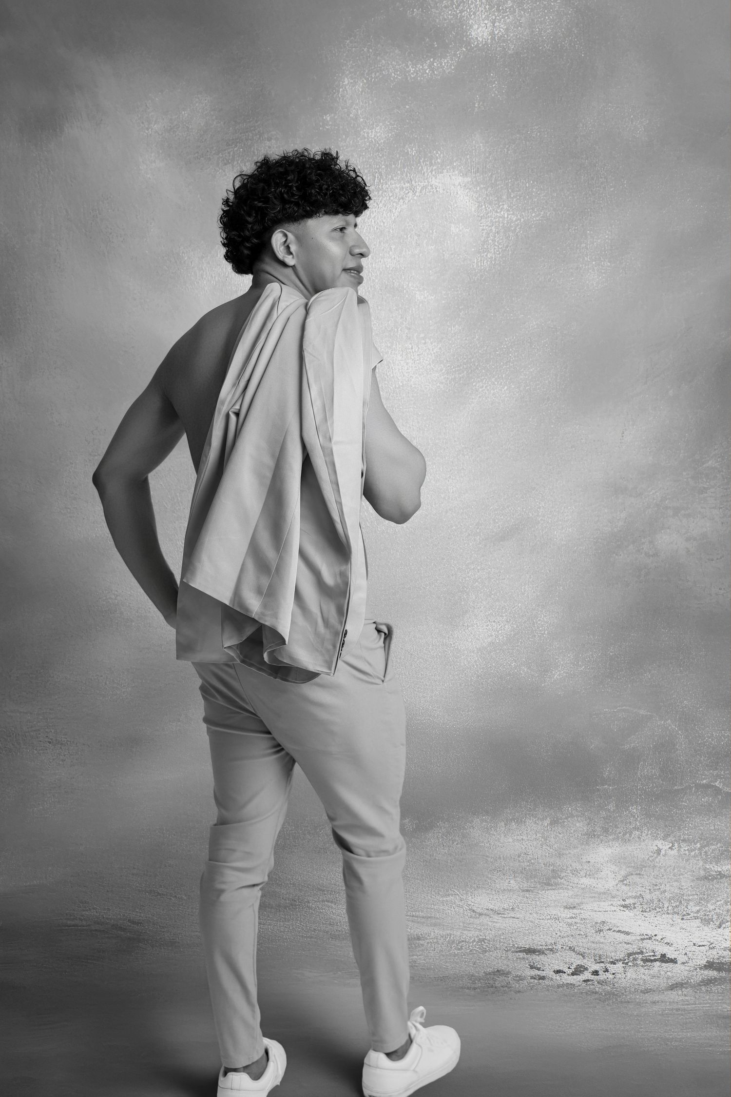 Black and white photo of a young man with curly hair, wearing a vest and trousers, holding a towel over his shoulder.
