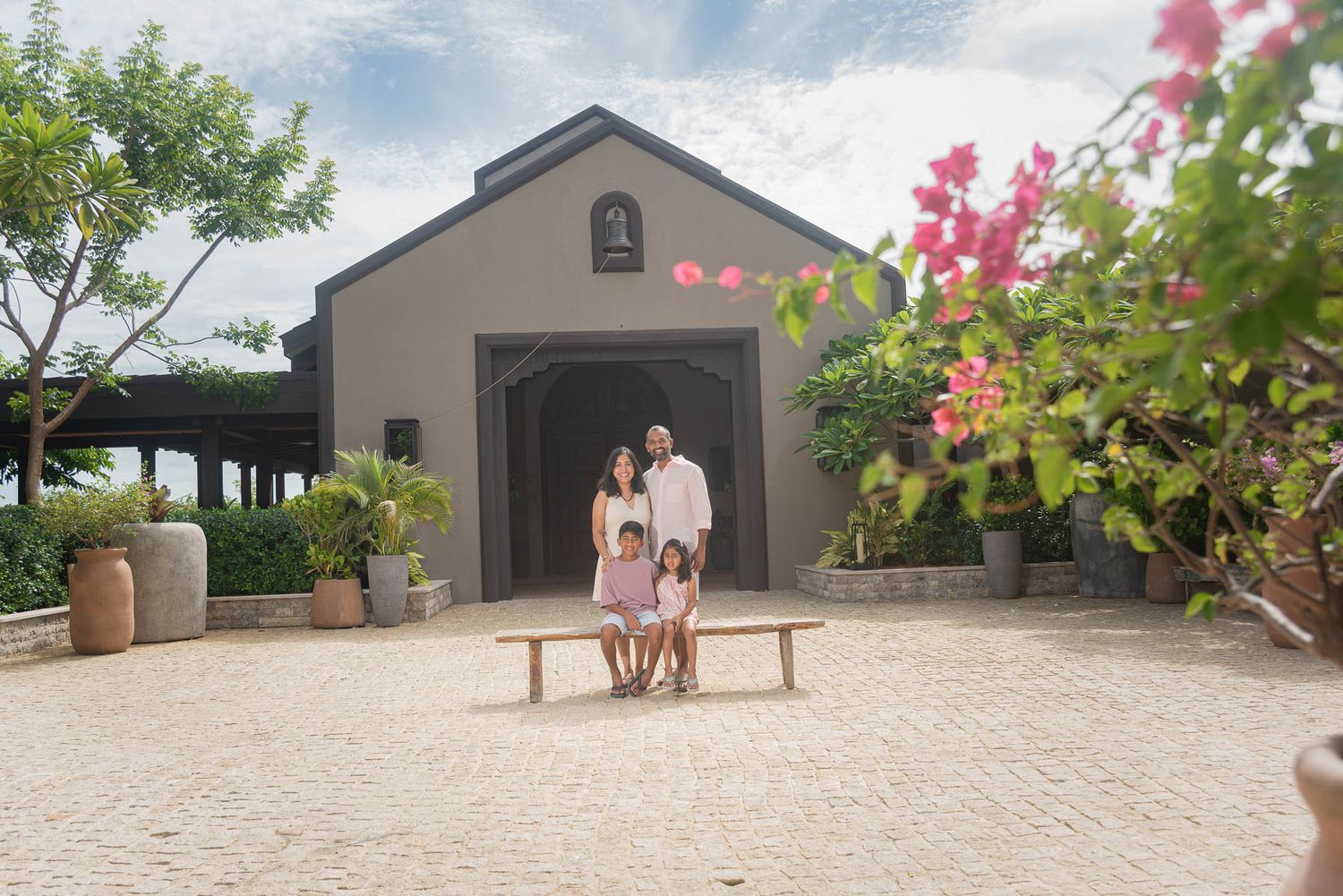 Family of three posing in front of a charming resort entrance surrounded by tropical gardens and bougainvillea.
