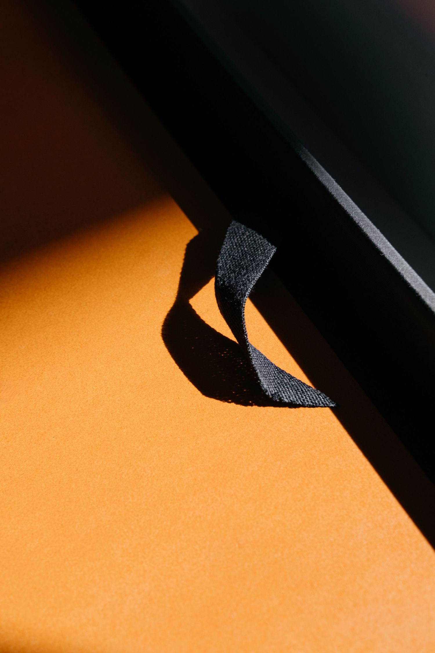 Black ribbon tag attached to dark frame corner casting shadow on orange surface in dramatic lighting.