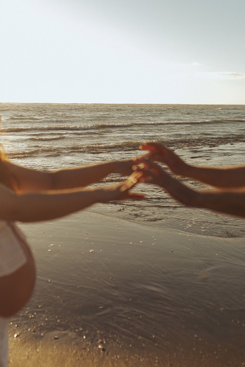 Couple holding hands on a sandy beach at golden sunset with ocean waves in the background at Waikato New Zealand beach.