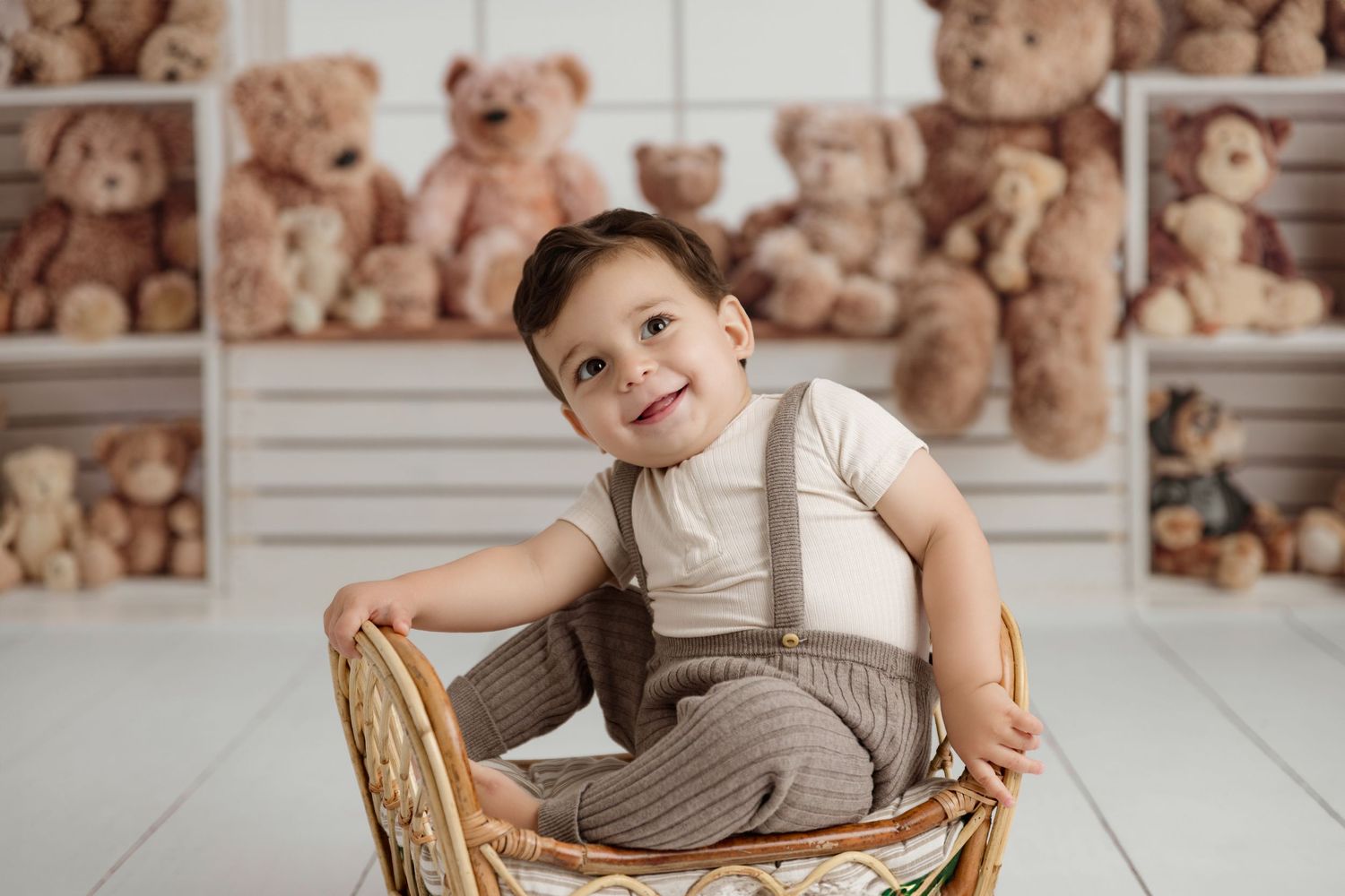 Smiling baby seated in a wicker chair in a teddy bear birthday set