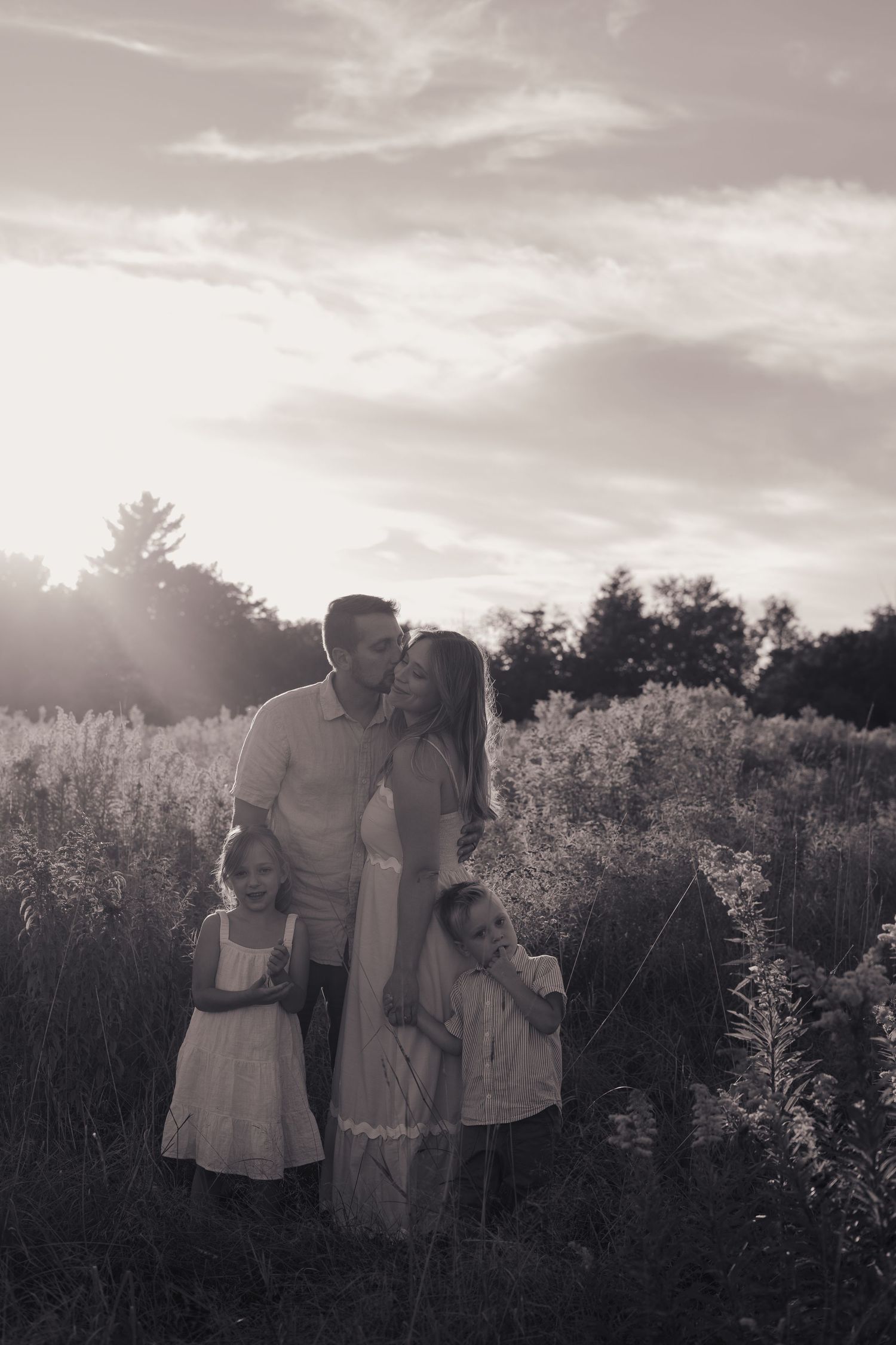 Family of four walking hand-in-hand on a lush green forest path surrounded by tall trees.
