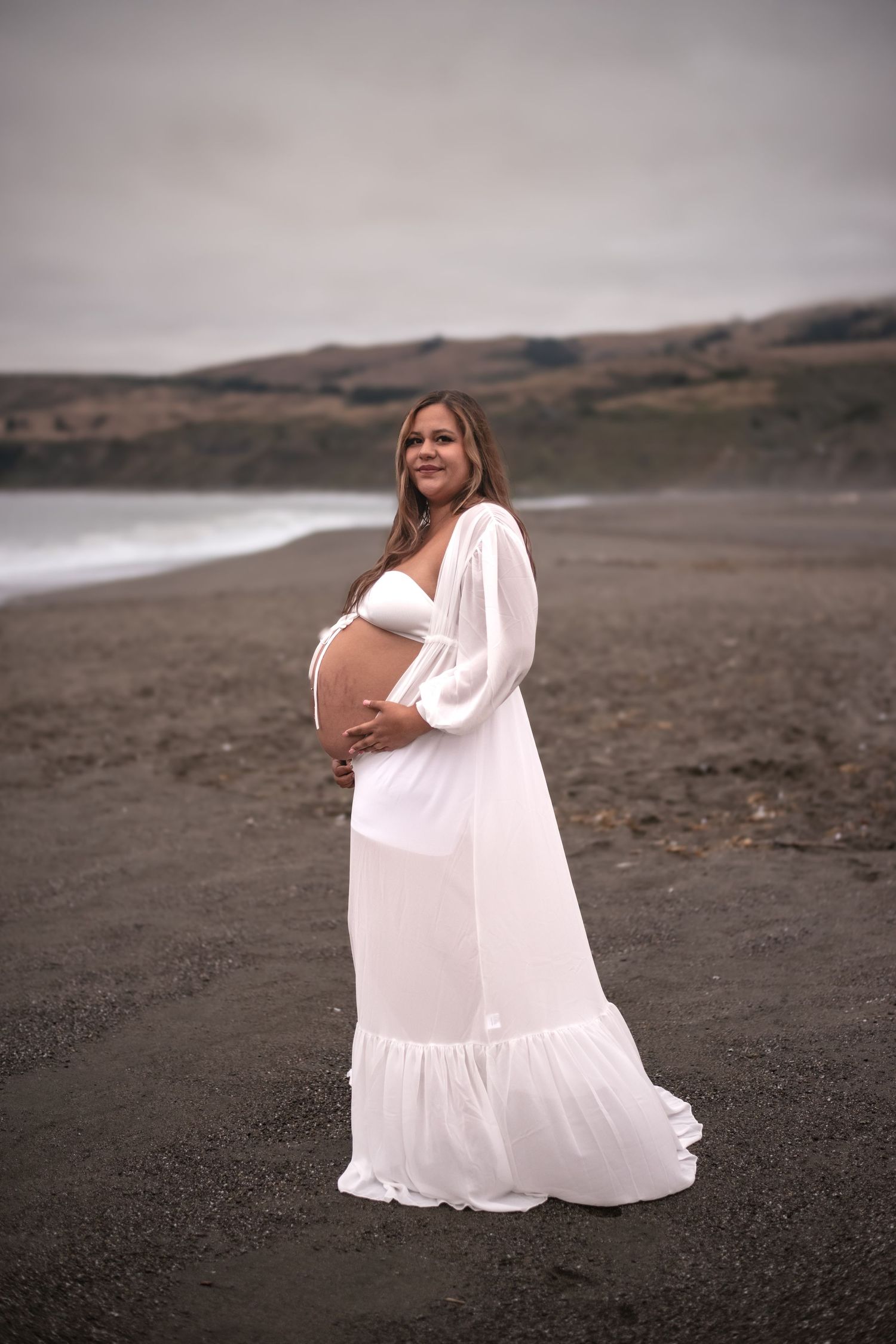 Cinematic maternity portrait of a woman at Goat Rock Beach, surrounded by rugged coastline, ocean air, and natural beauty.