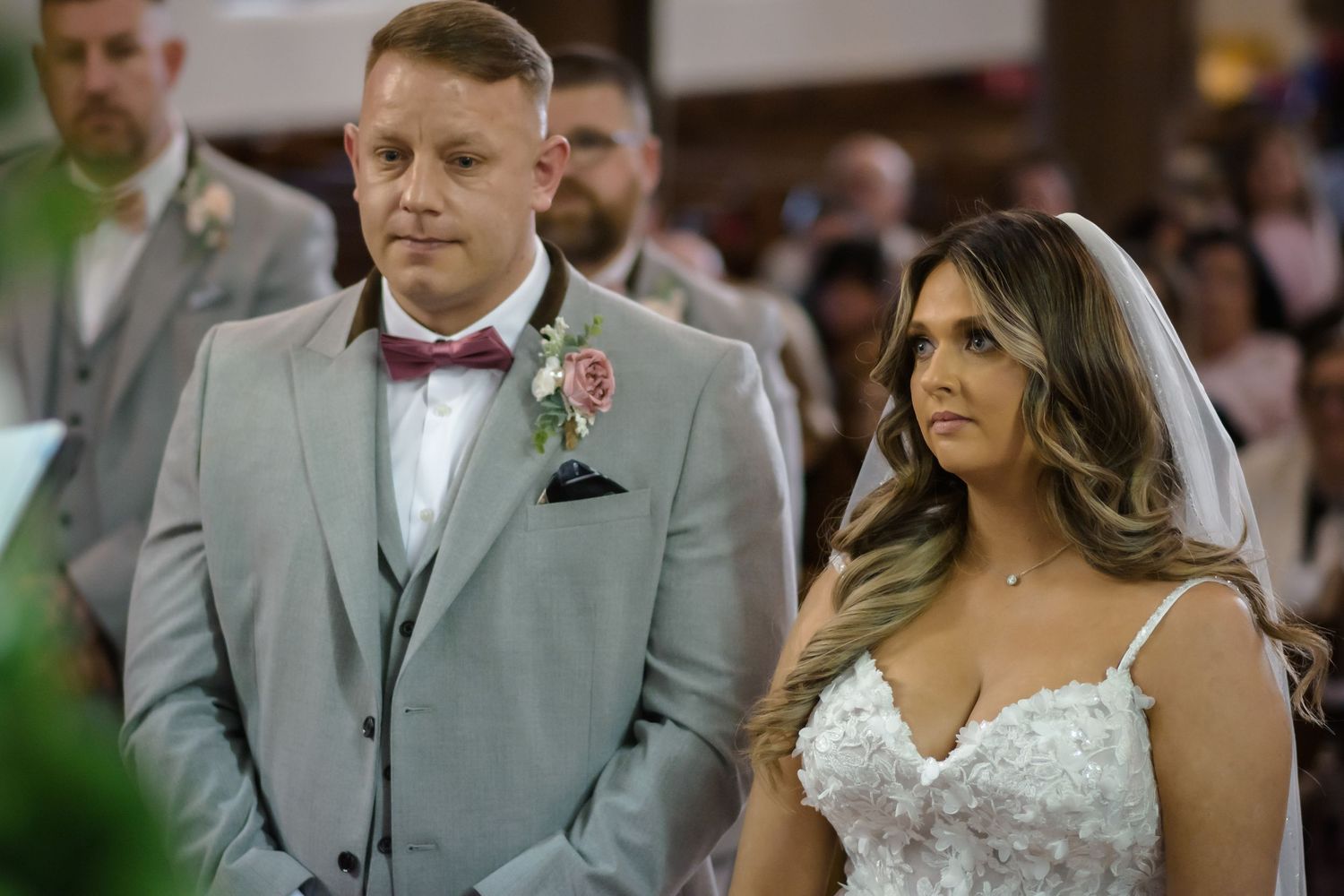 A bride and groom stand at the altar during their wedding ceremony, dressed in elegant attire.
