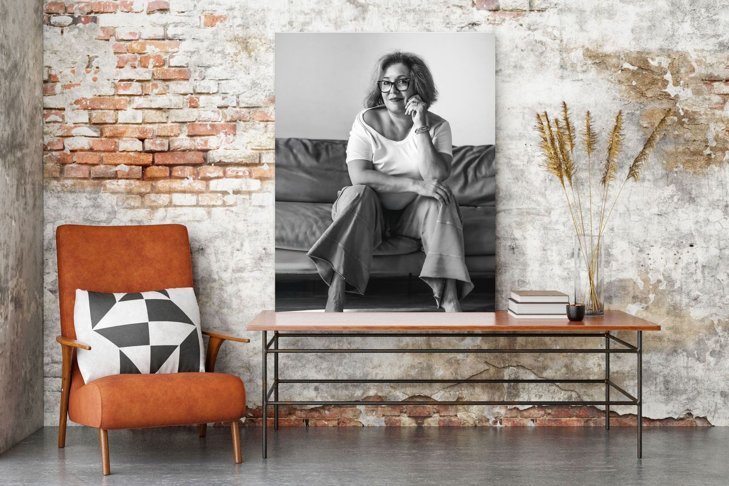 Black and white photo print of a woman sitting on a couch, displayed on a brick wall above a wooden table.