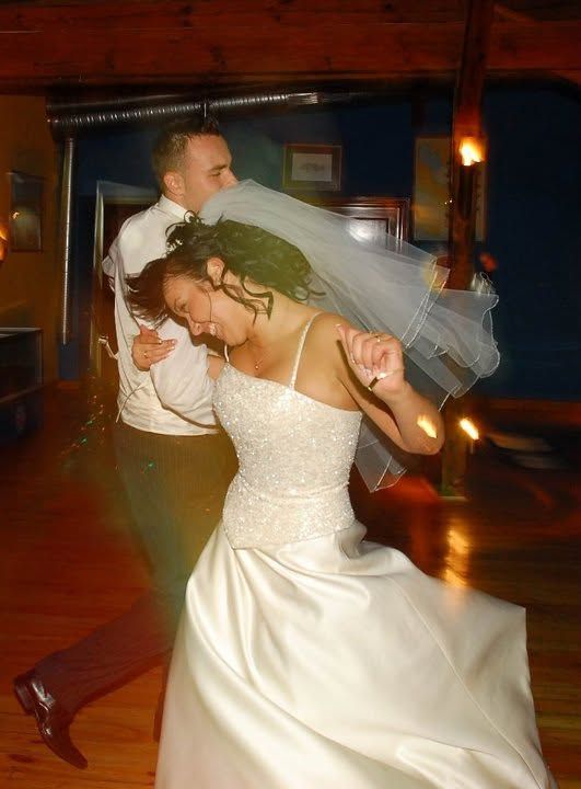 Bride and groom share their first dance, with the bride in a white gown and veil, twirling on a warmly lit dance floor.