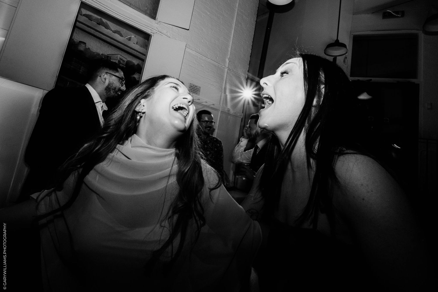 Two women laughing joyfully together at a party in a black and white photo.