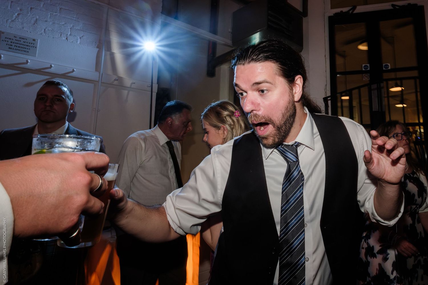 Excited man in vest and tie reacting with surprise at a lively indoor event or wedding reception.
