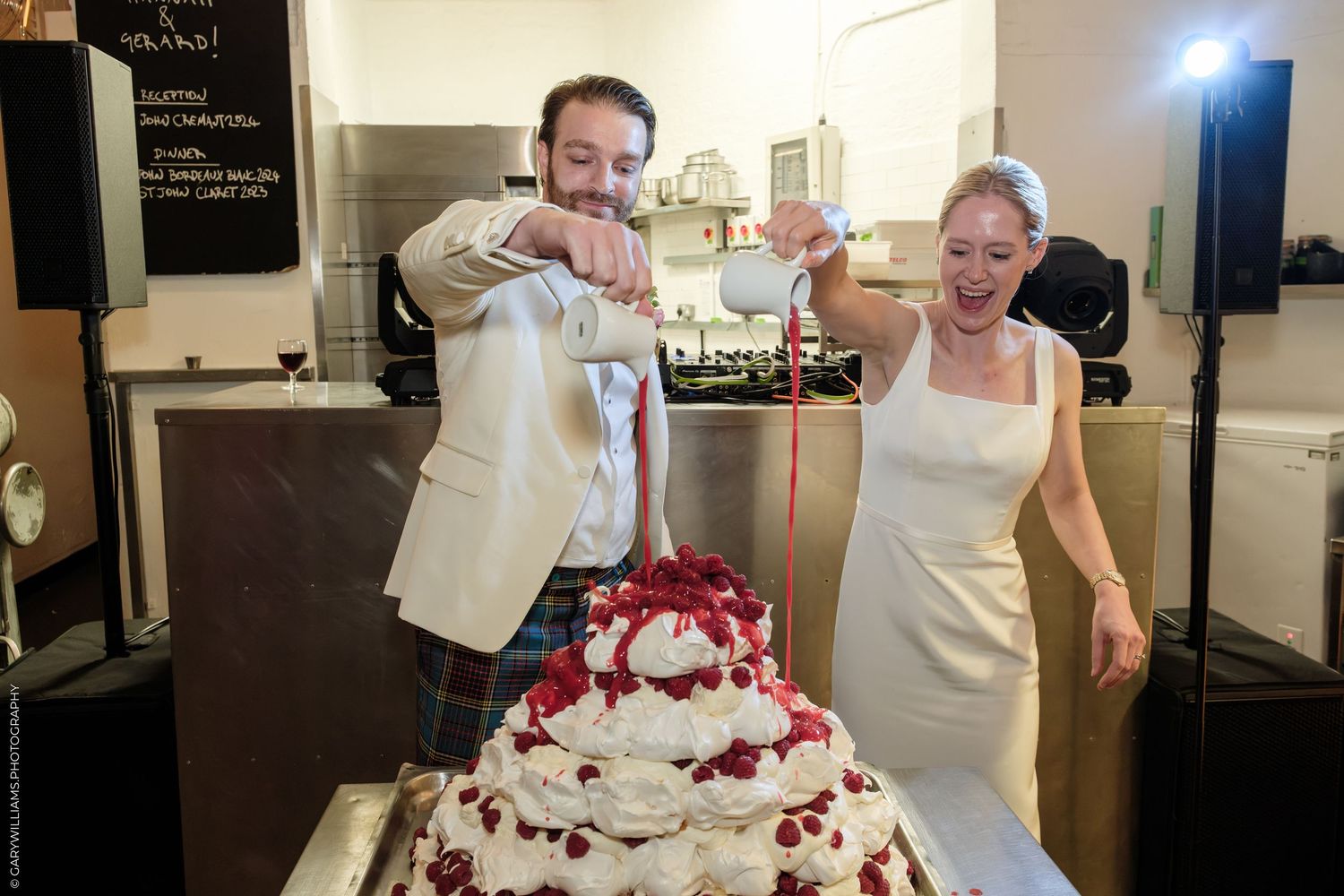 Bride and groom cutting a white wedding cake decorated with red berries at their wedding reception.