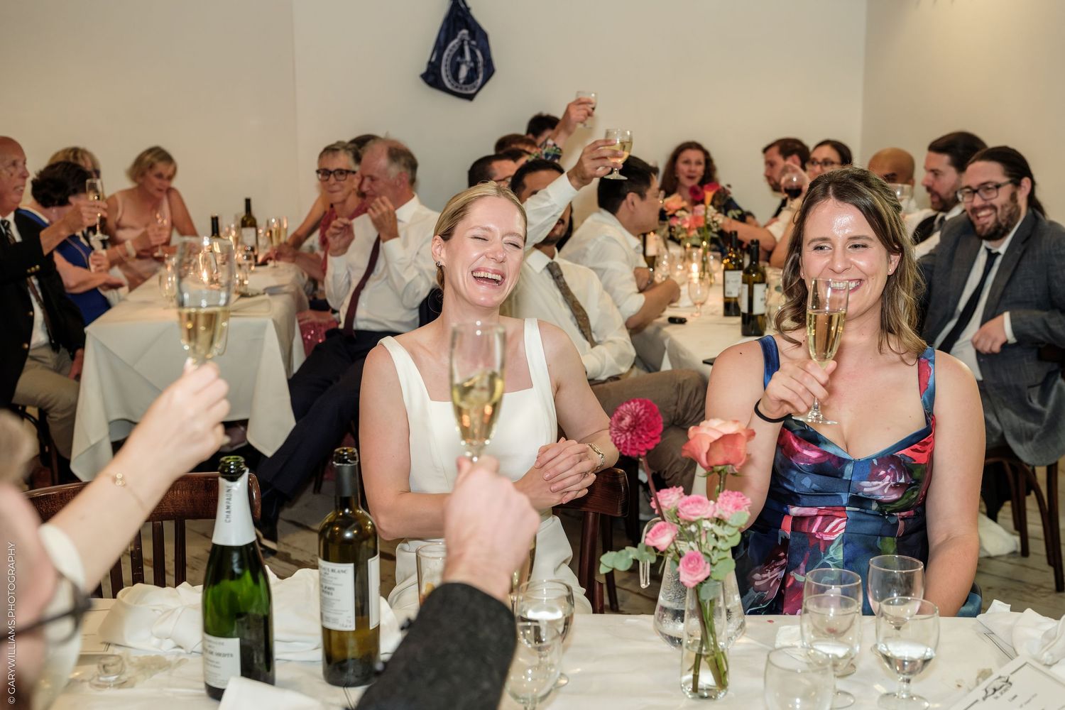 Bride and guests laughing and toasting with champagne glasses at a wedding reception dinner.