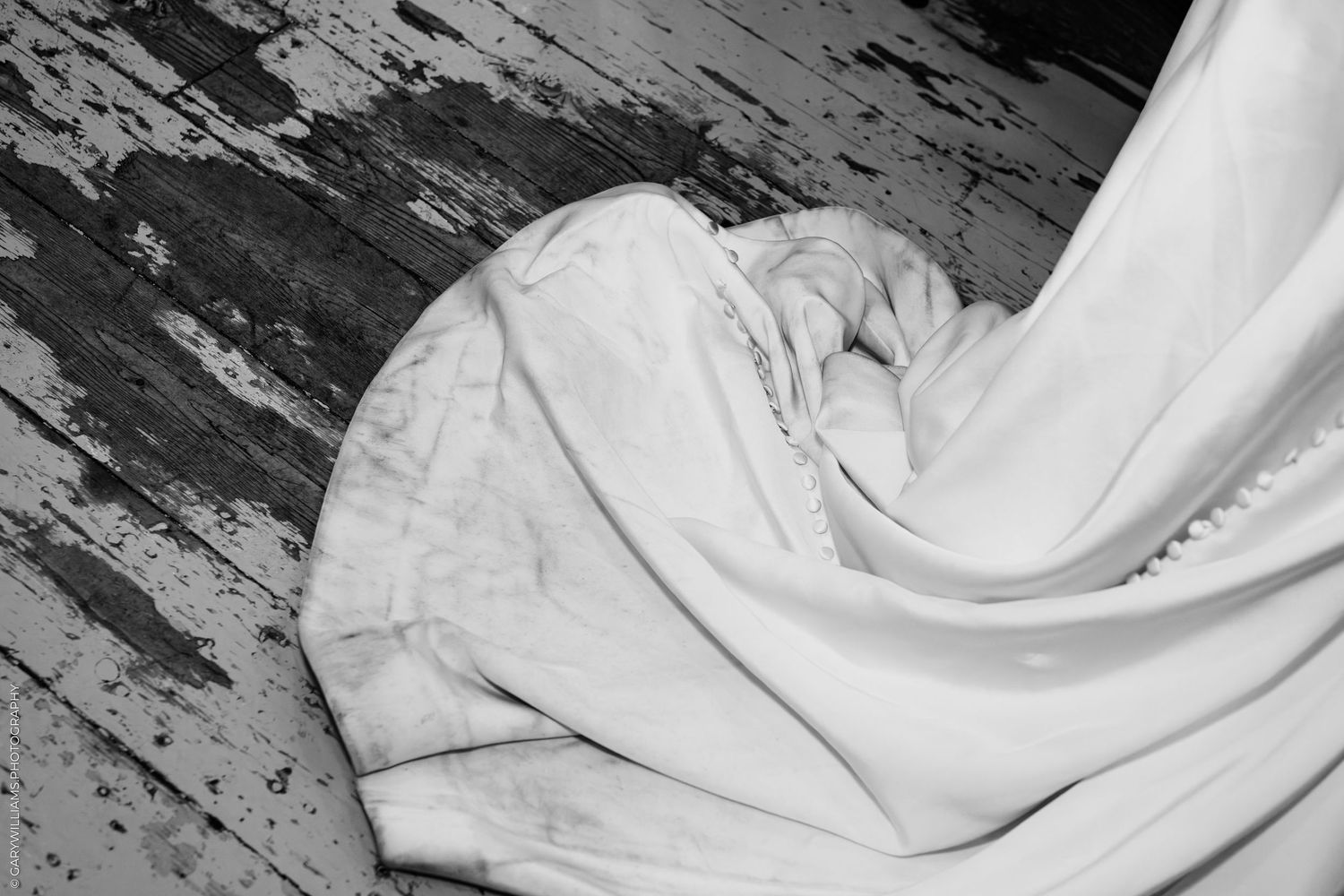 Black and white photo of white fabric draped on a weathered wooden floor with peeling paint.