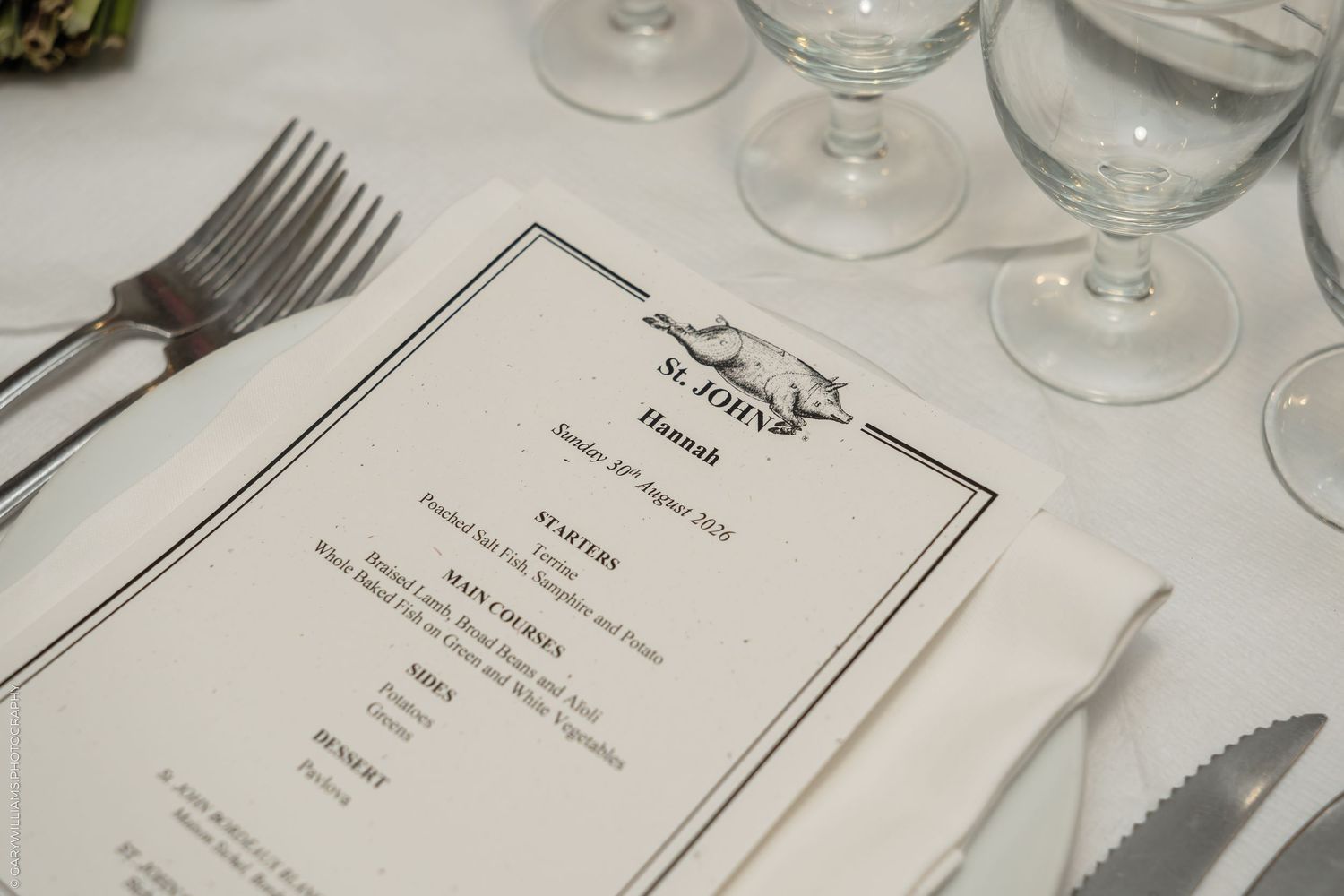 Elegant place setting at St. John restaurant with a formal dinner menu card, silverware, and crystal glassware on white tablecloth.
