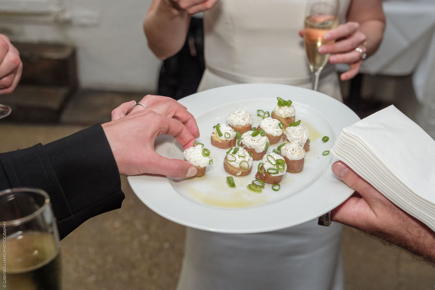Server presenting elegant appetizers on white plate with cream topping and green onions at event.