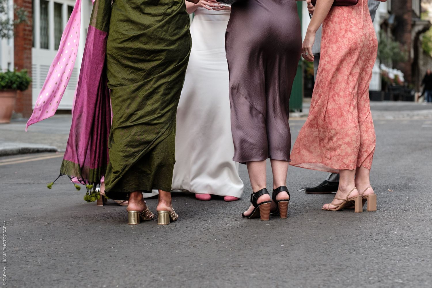 Four women in elegant maxi dresses and heels walk together on a city street, showcasing colorful formal attire.