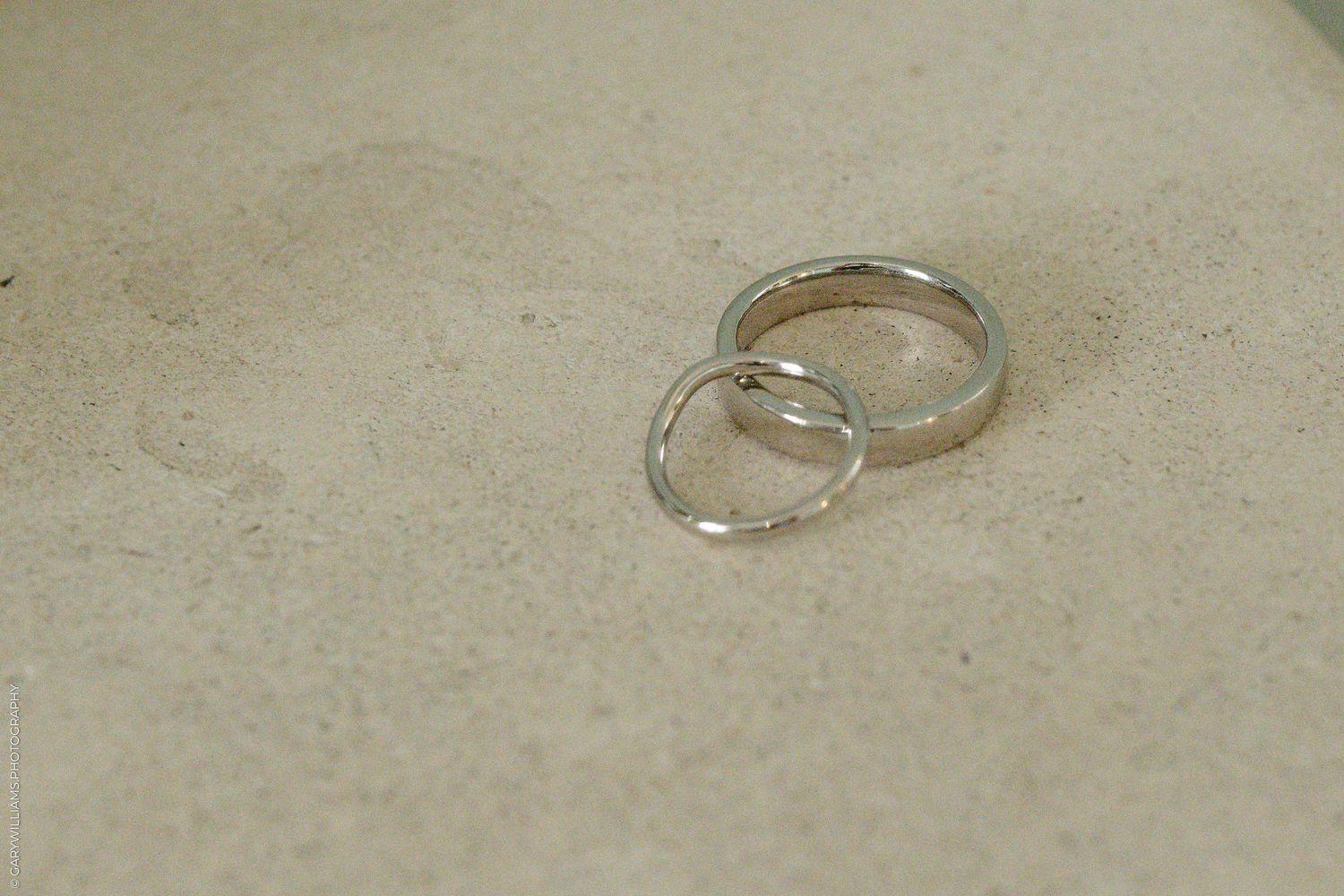 Two silver wedding bands resting on a beige stone surface, symbolizing marriage and commitment.