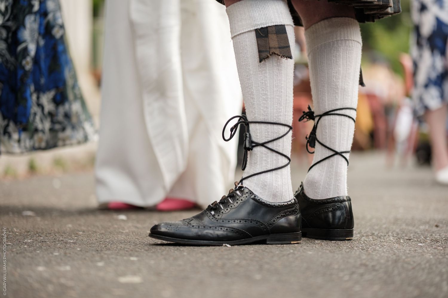 Close-up of traditional Scottish Highland dress shoes with lace-up ribbons and white knee-high socks on pavement.