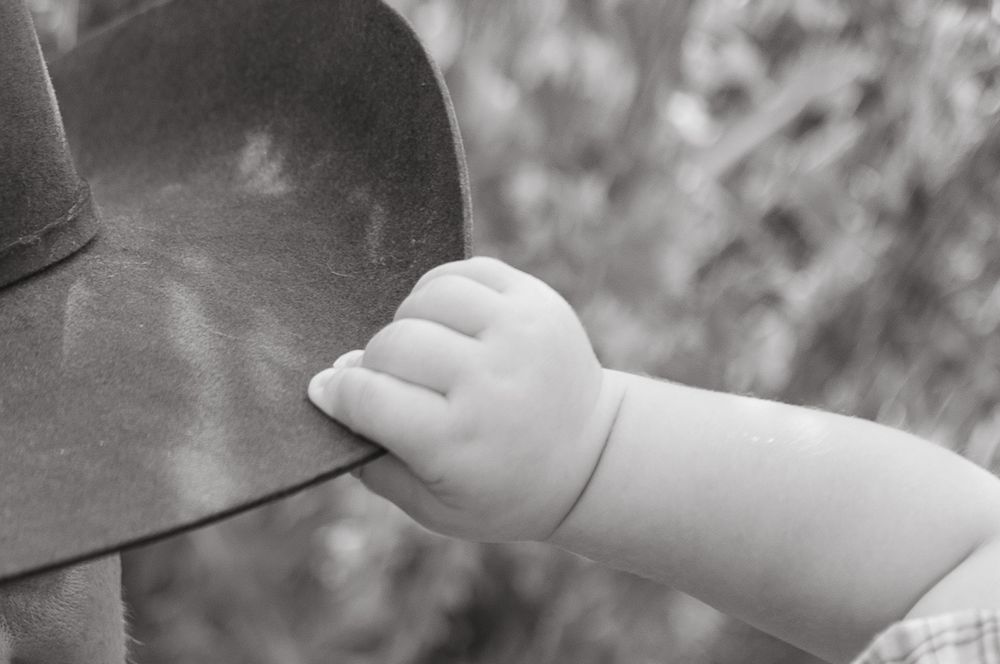 Black and white close-up of a baby's tiny hand gently gripping an adult's clothing outdoors.