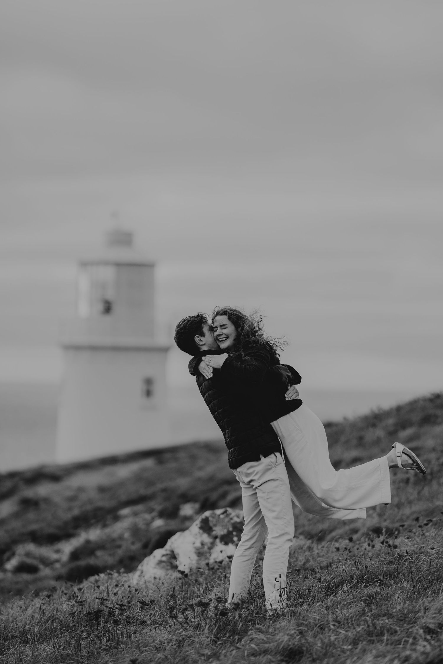 Black and white photo of a couple embracing and kissing near the lighthouse at trevose head.