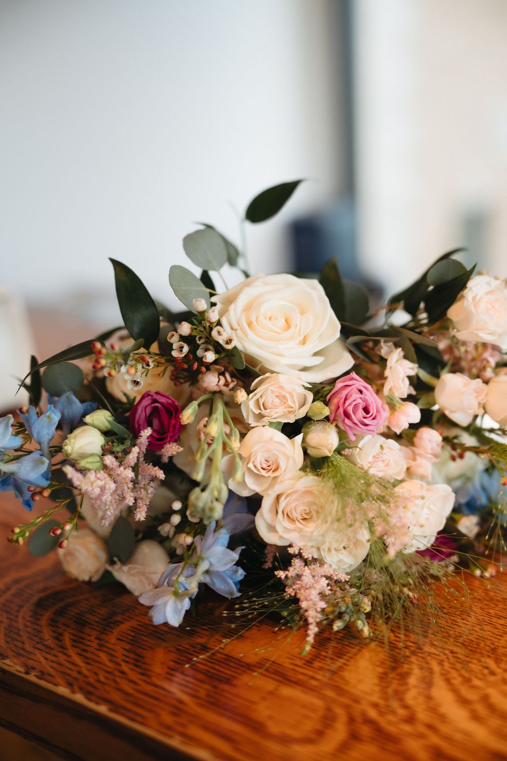 Elegant wedding bouquet with cream, pink roses, blue flowers, and greenery on a wooden table.