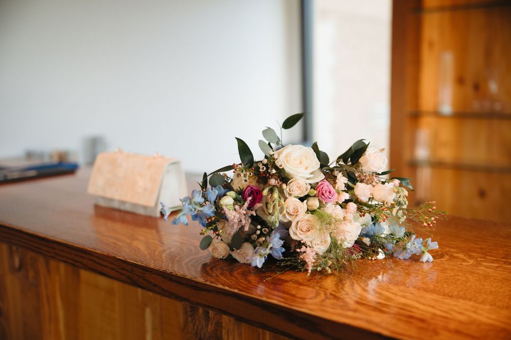 Elegant wedding floral arrangement with pink roses and blue flowers on a wooden surface.