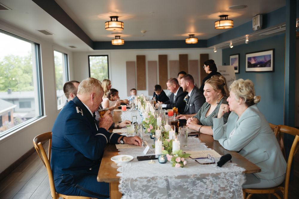 Guests seated at a decorated banquet table during a formal dinner event in a bright restaurant with large windows.
