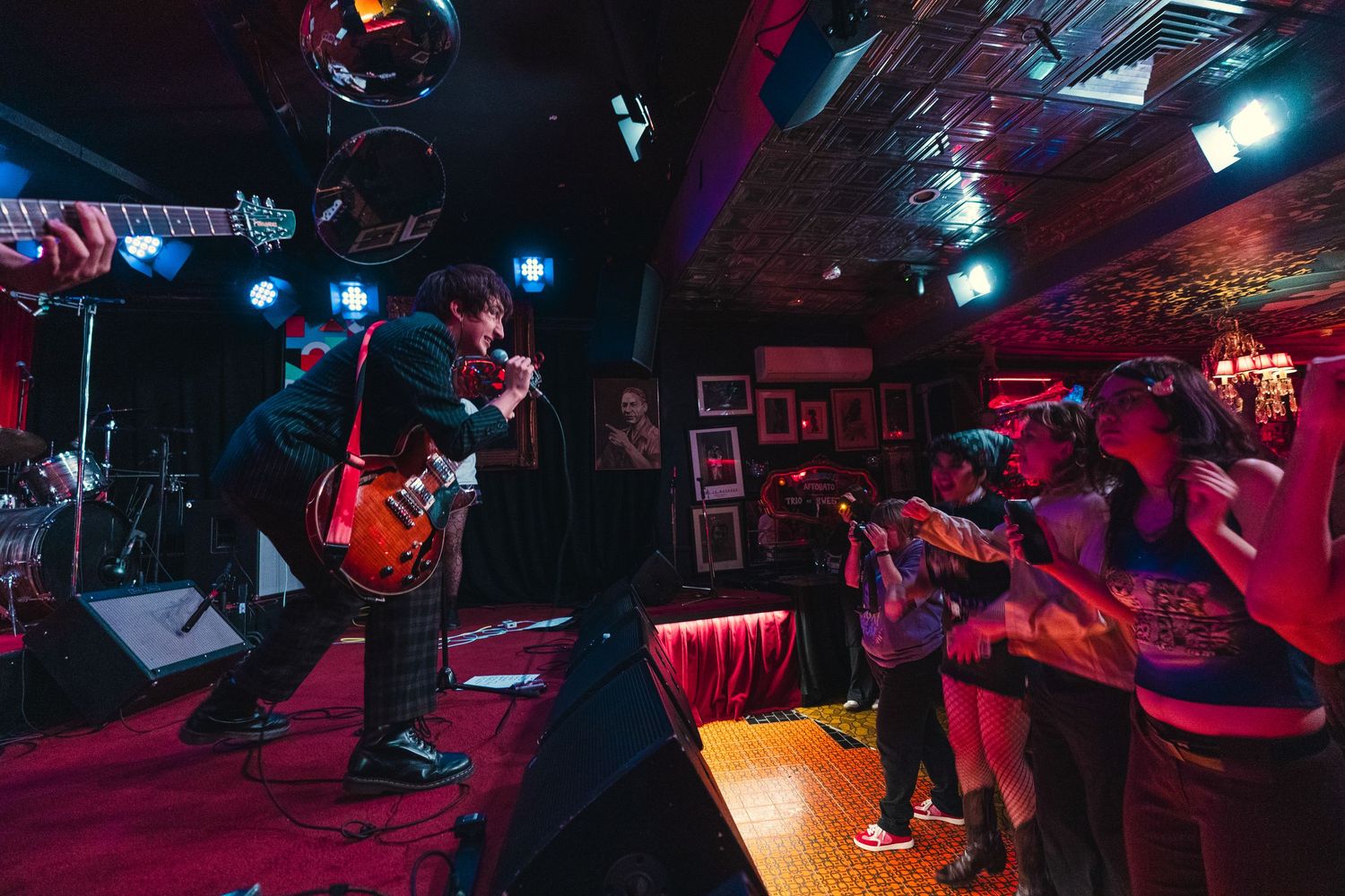Rock band performs live on stage with red and blue lights as excited crowd watches from below.