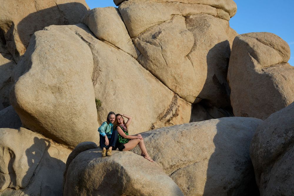 Two women posing together on large granite boulders in Joshua Tree National Park on a sunny day.
