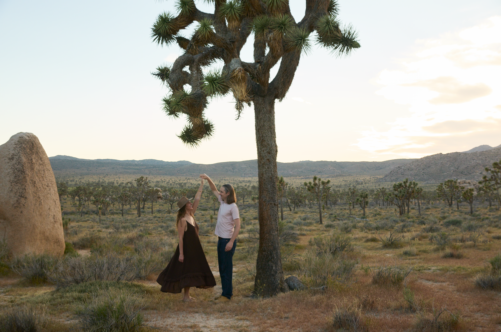 Two women dancing near a Joshua tree in the scenic desert landscape of Joshua Tree National Park at sunset.
