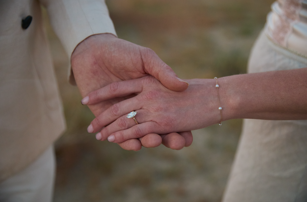 Close-up of couple holding hands, bride wearing diamond engagement ring and delicate bracelet at wedding.