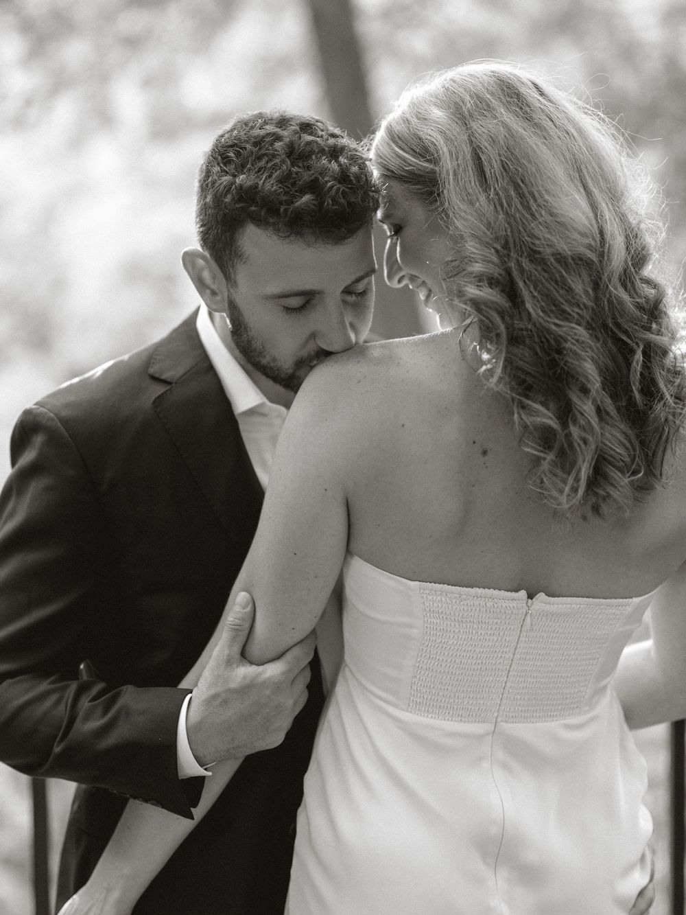 Black and white photo of groom kissing bride on shoulder tenderly.