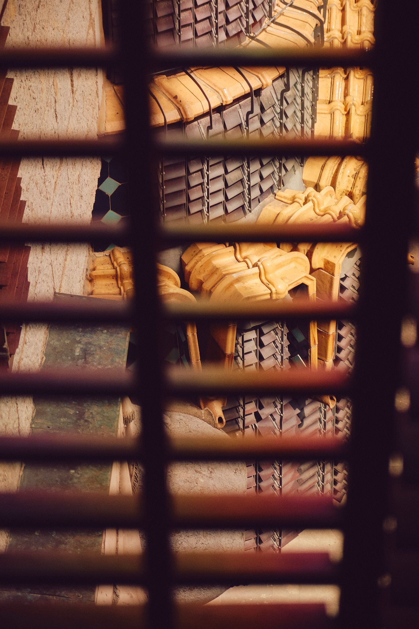 Aerial view through wooden slats of people gathered in an ornate lobby with parquet floors and vintage wall sconces.