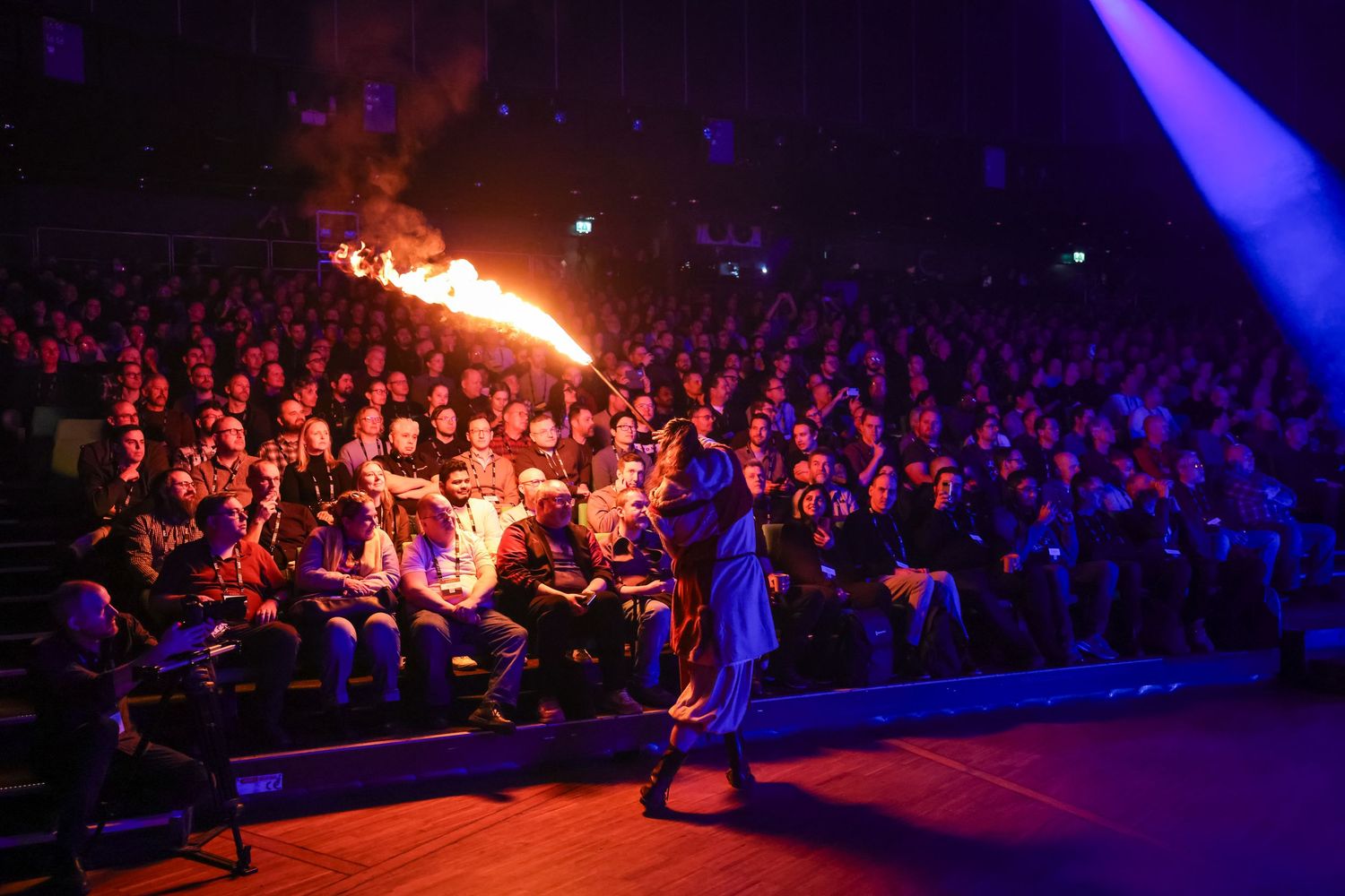 Fire performer entertaining a large crowd at a spectacular indoor tech conference evening event.