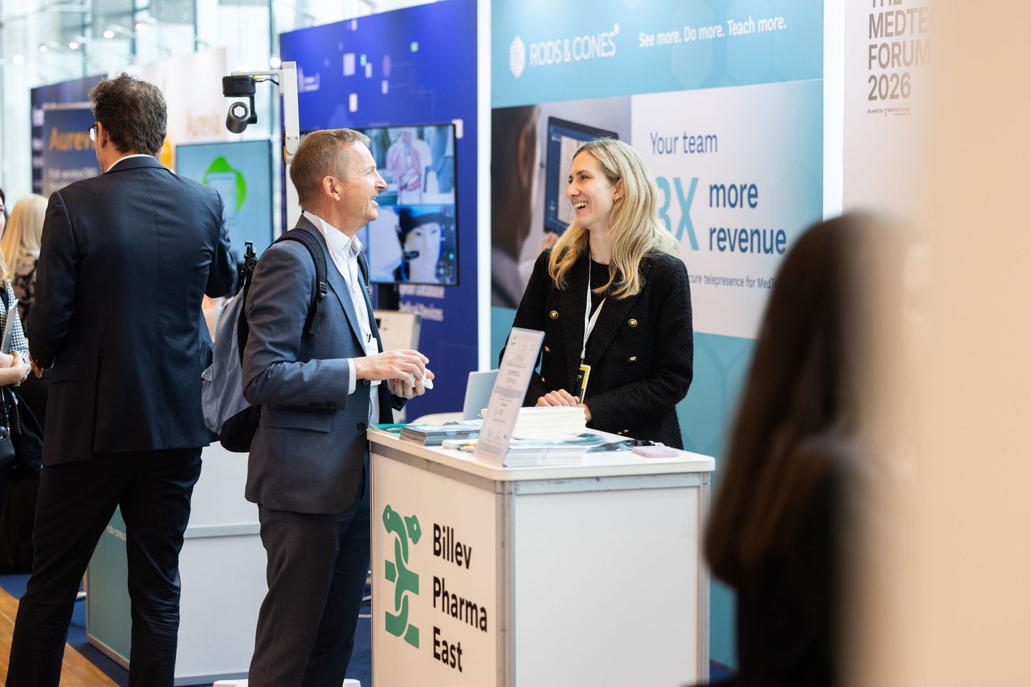 Blonde woman representing Bilev Pharma East speaking with attendees at a pharmaceutical conference booth.