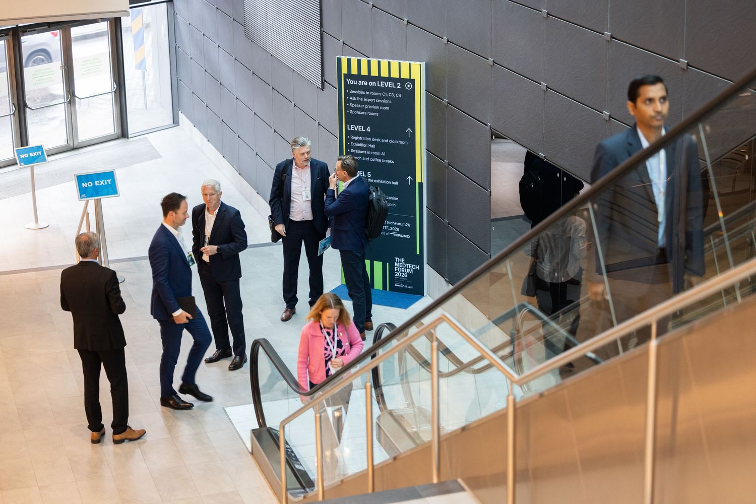 Business professionals networking in a modern conference center lobby near escalators.