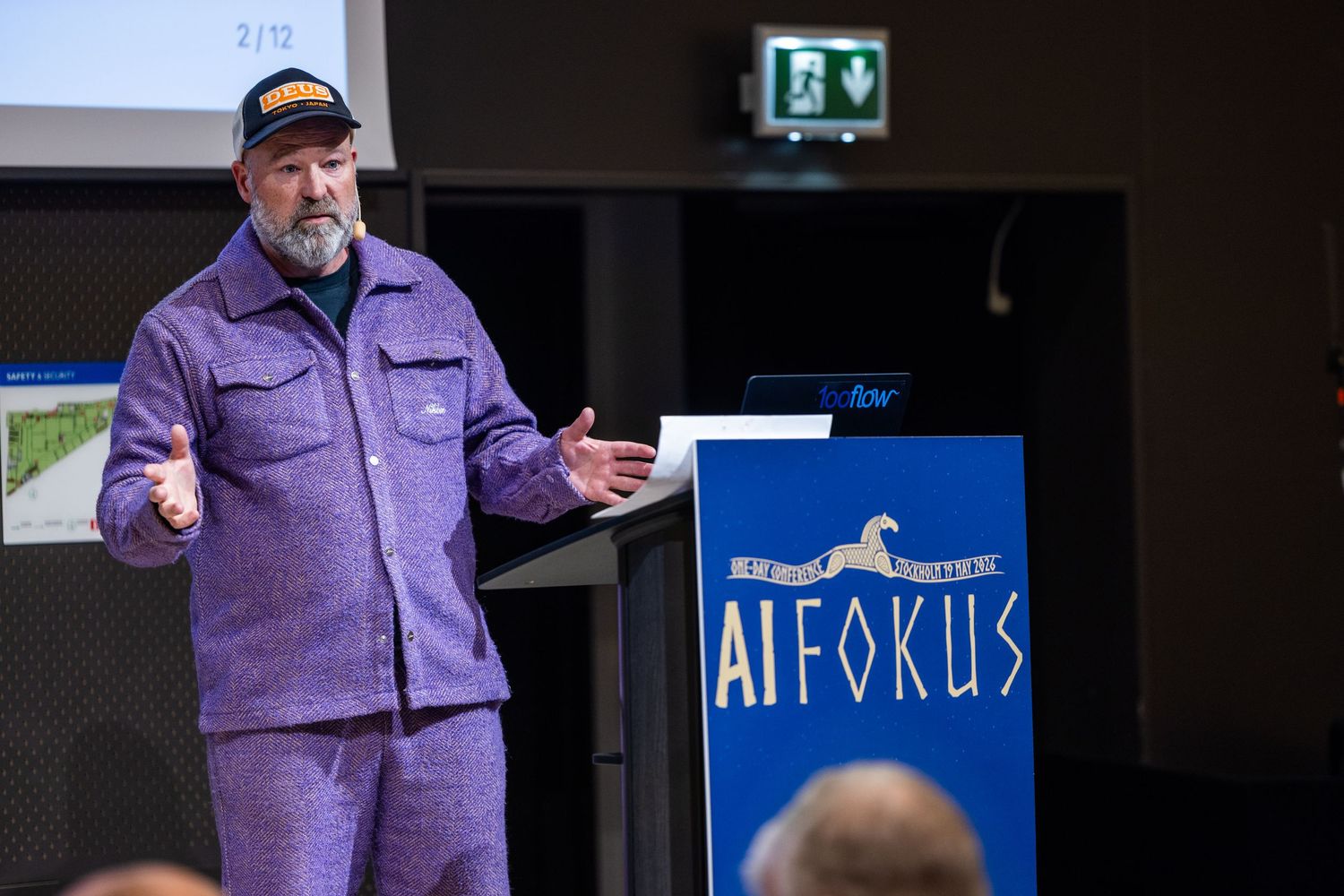 Speaker in purple suit presenting at AI Fokus conference podium on stage.