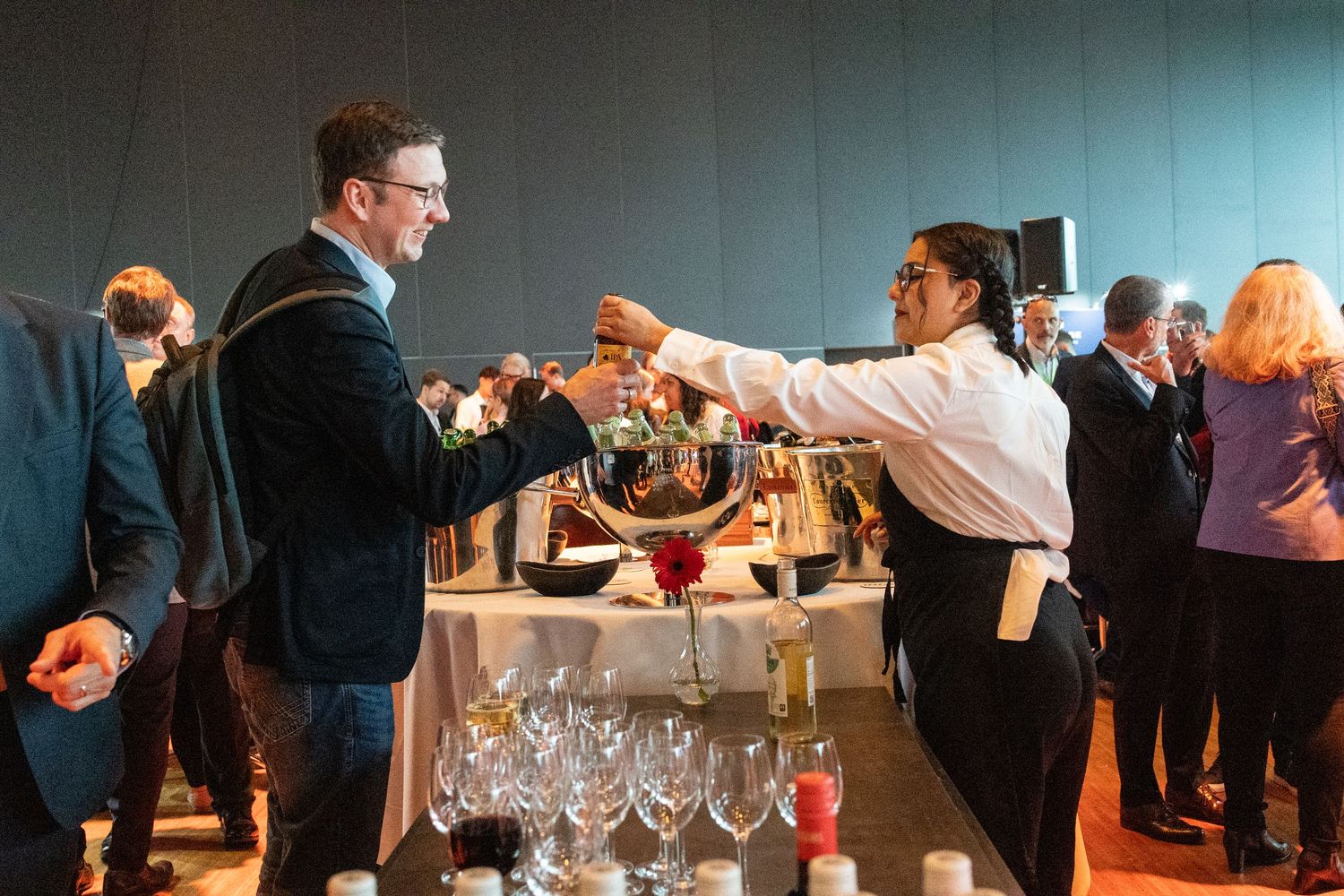 A server pouring red wine for a guest at an elegant indoor reception event.