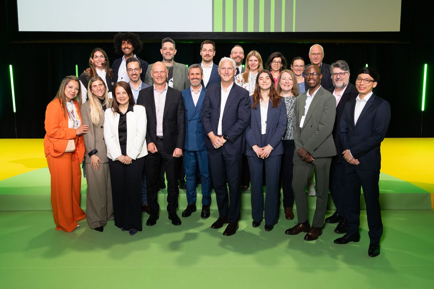 Group of professionals posing together on a green stage at a corporate conference event.