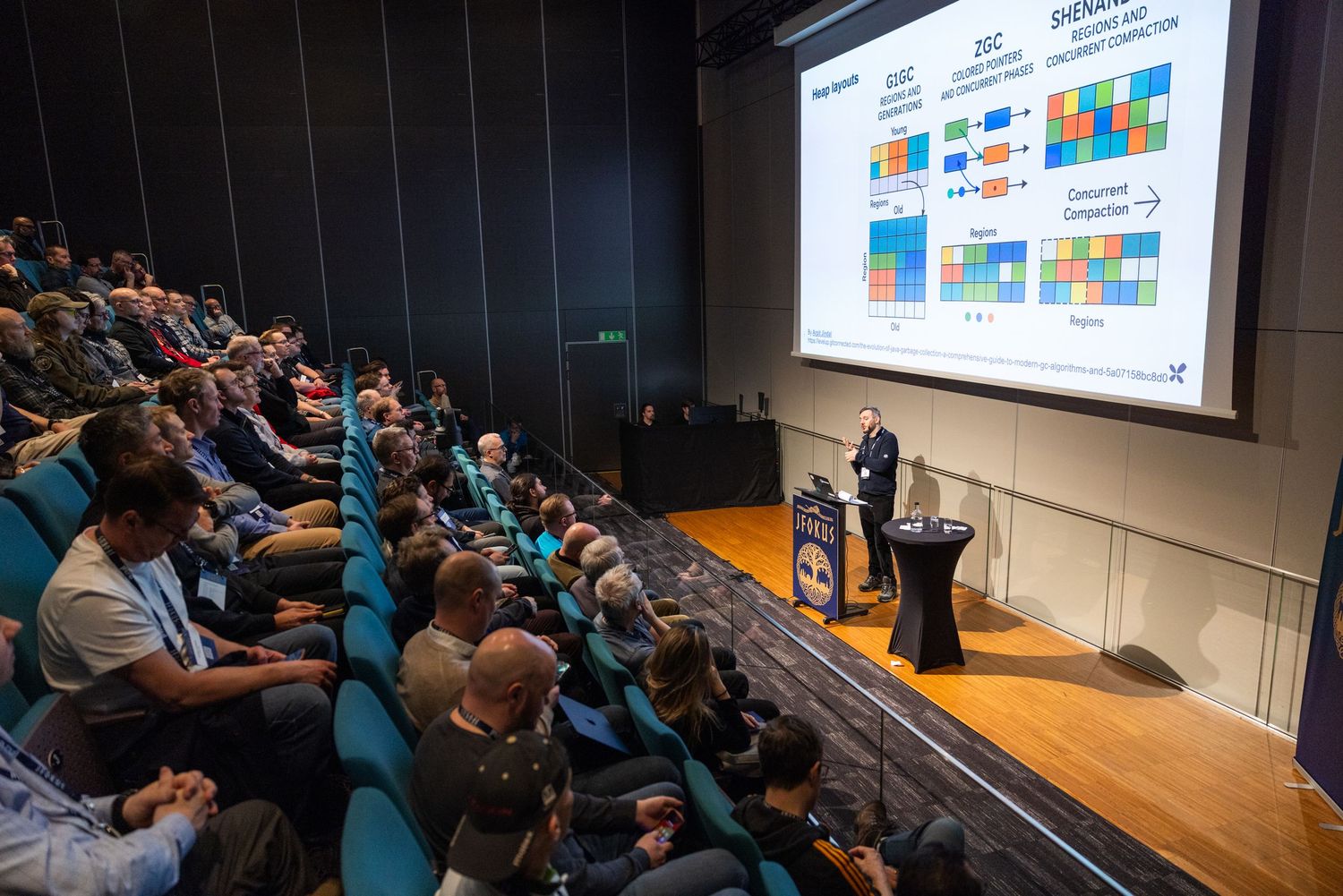 Speaker presenting colorful data slides to an engaged audience in a darkened conference hall.