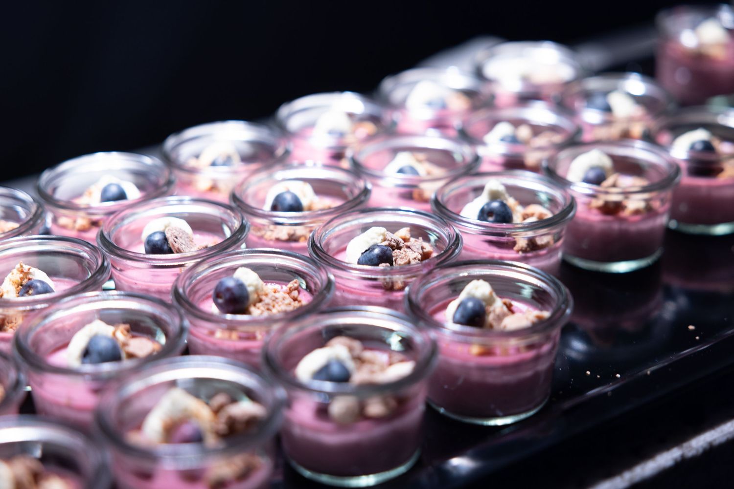 Elegant blueberry mousse desserts in glass cups garnished with fresh berries and granola.