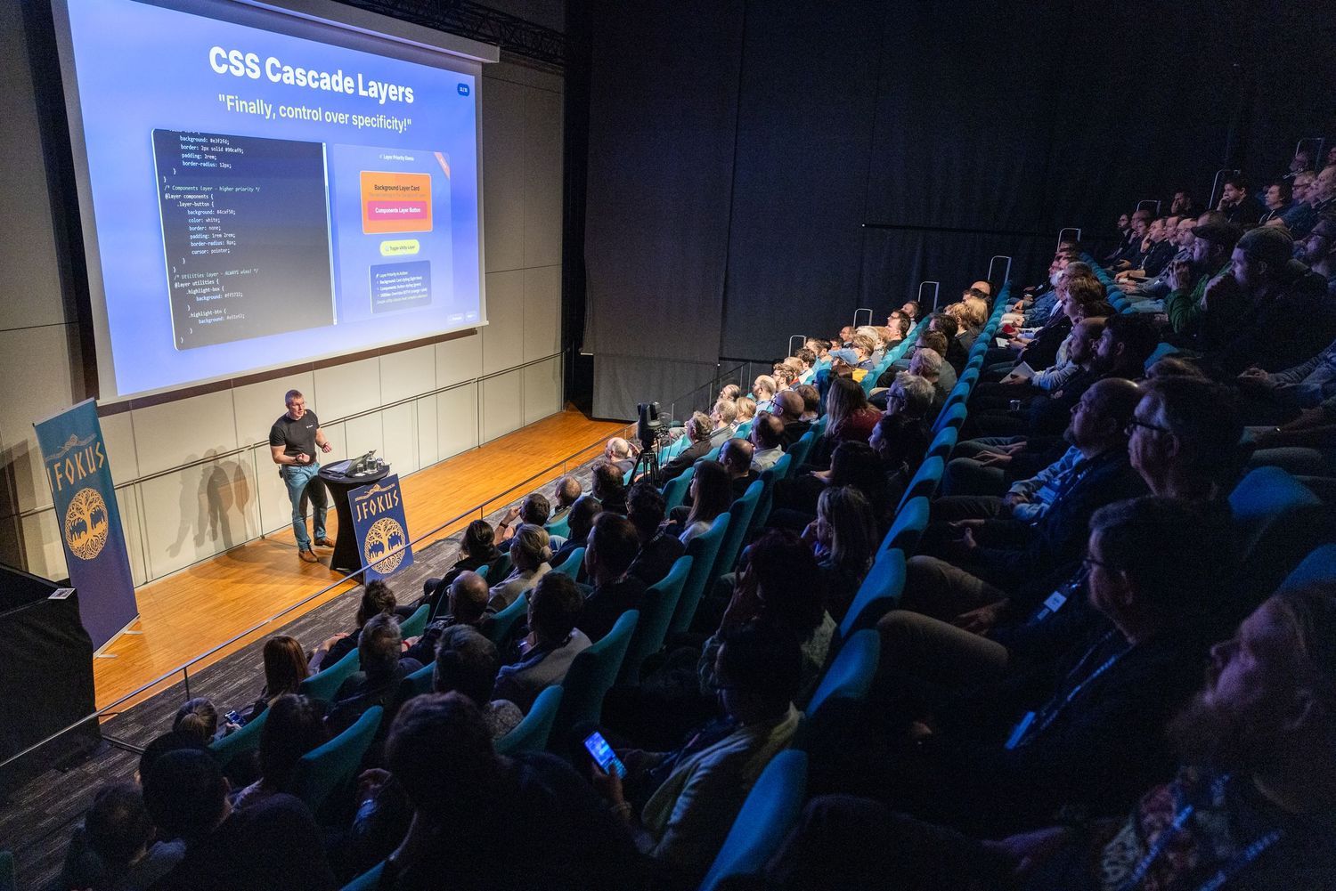 Large audience attending a CSS Cascade Layers presentation in a darkened conference auditorium.