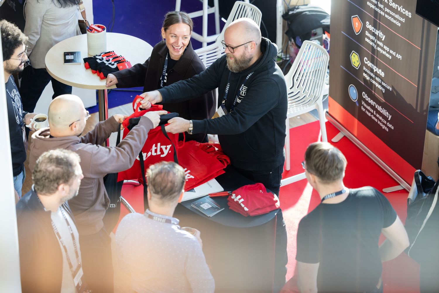 Attendees receiving red branded merchandise at a tech conference exhibition booth.